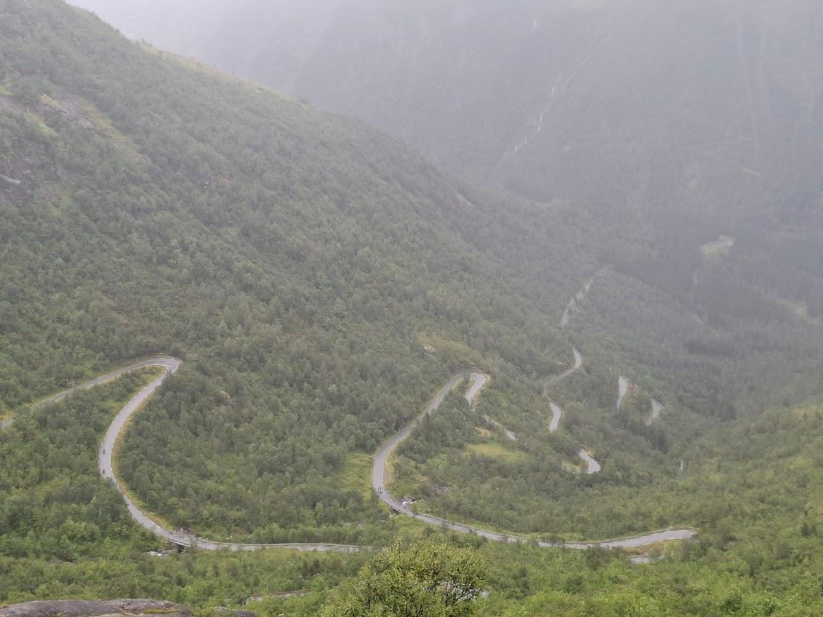 Winding mountain road with switchbacks through dense green forest under foggy conditions