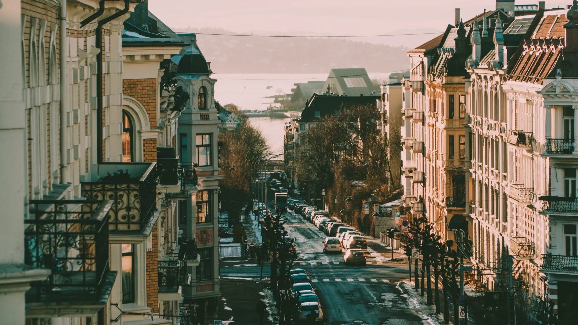 Street view in Oslo with historic buildings leading toward a waterfront and hills.